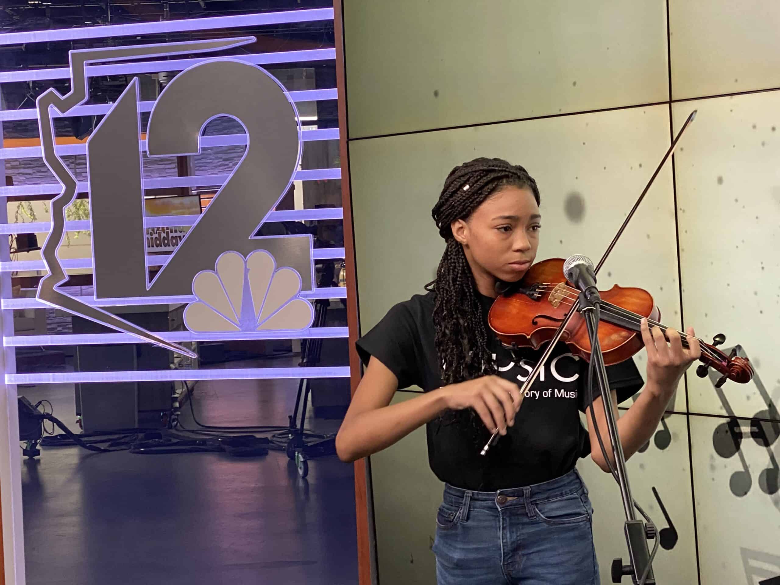 Music student Avi Calloway playing violin in front of a microphone with the 12 News logo in the background.