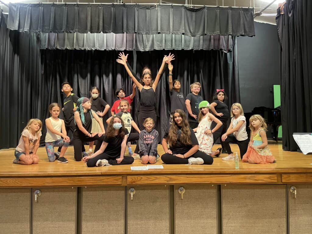 A group of kids, ages 9-13, posing on stage as part of PCM's summer camp in 2022 called Bravo for Broadway.
