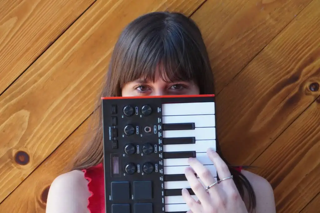 Photo of dark haired woman holding a midi keyboard over the bottom half of her face.