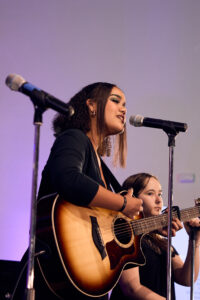 Young female singer strumming a guitar in front of a microphone.